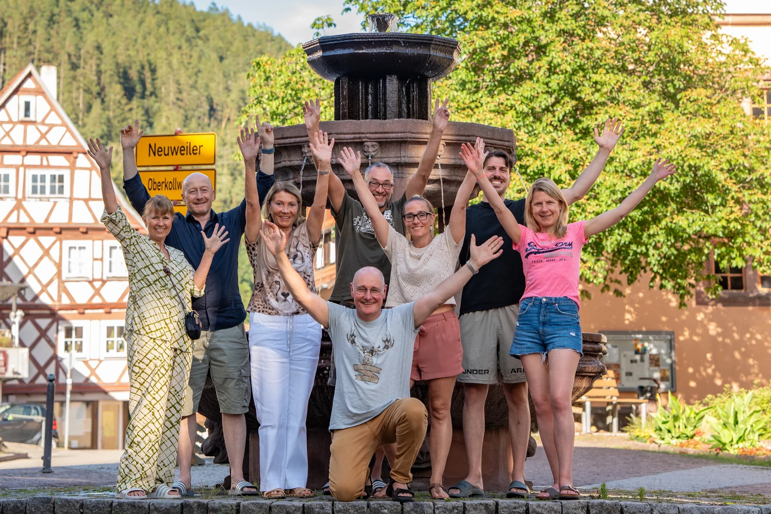 Fröhliche Fastengruppe mit erhobenen Armen vor einem Dorfbrunnen im Schwarzwald