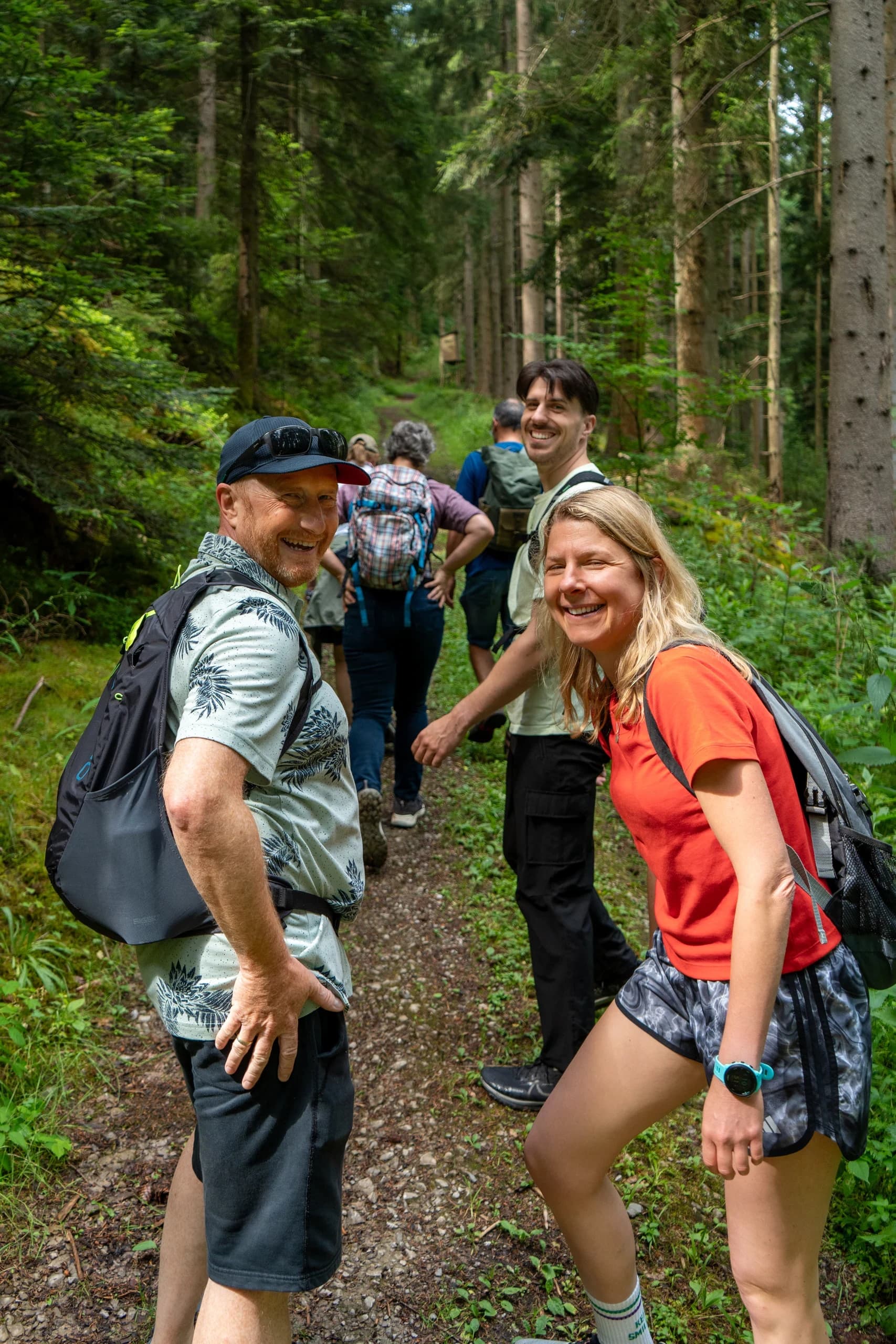 Zwei lachende Wandernde auf einem Waldweg im Schwarzwald, dahinter die Gruppe
