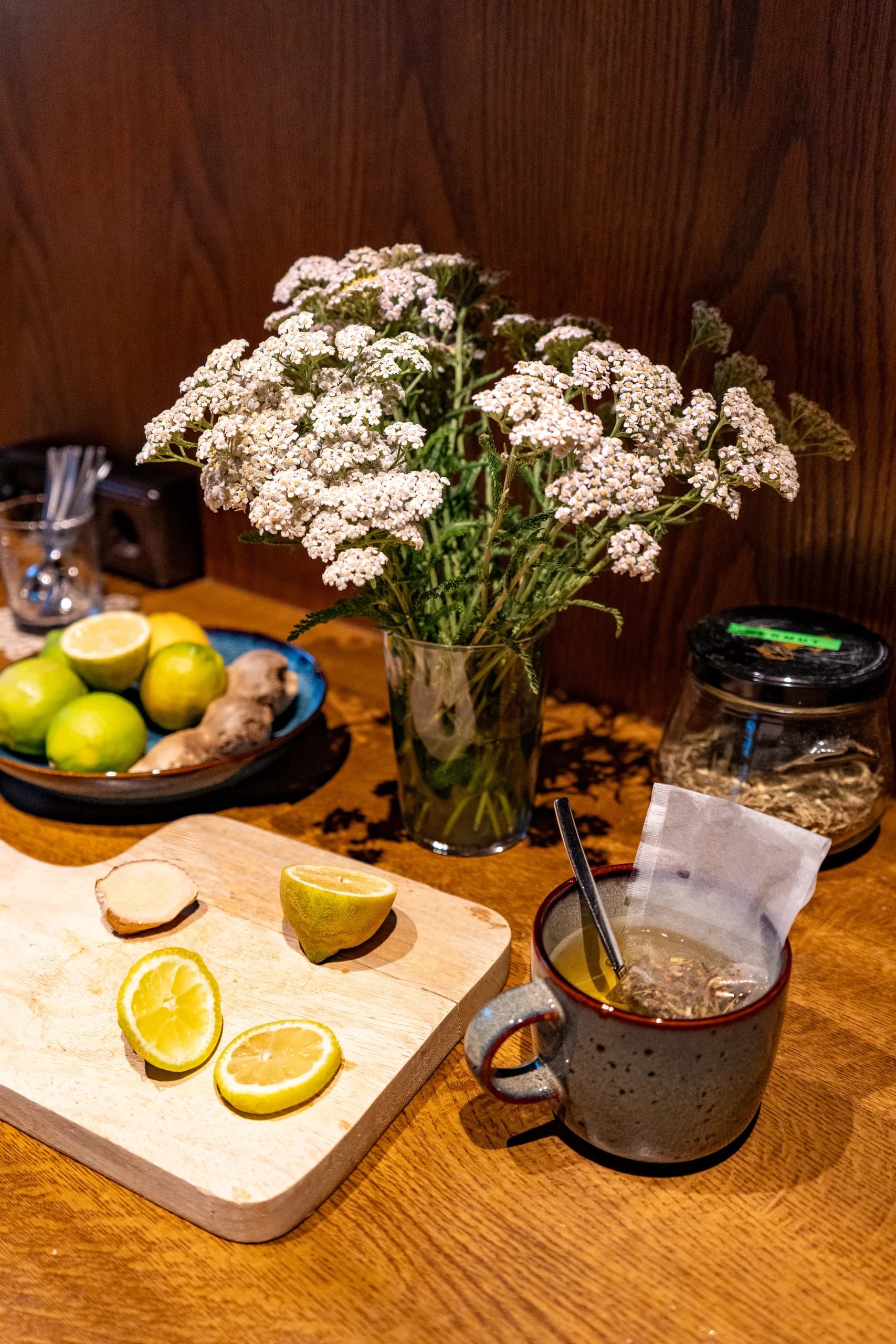Wildblumenstrauß, Zitronen und Ingwer auf einem Holzbrett neben einer Tasse Tee